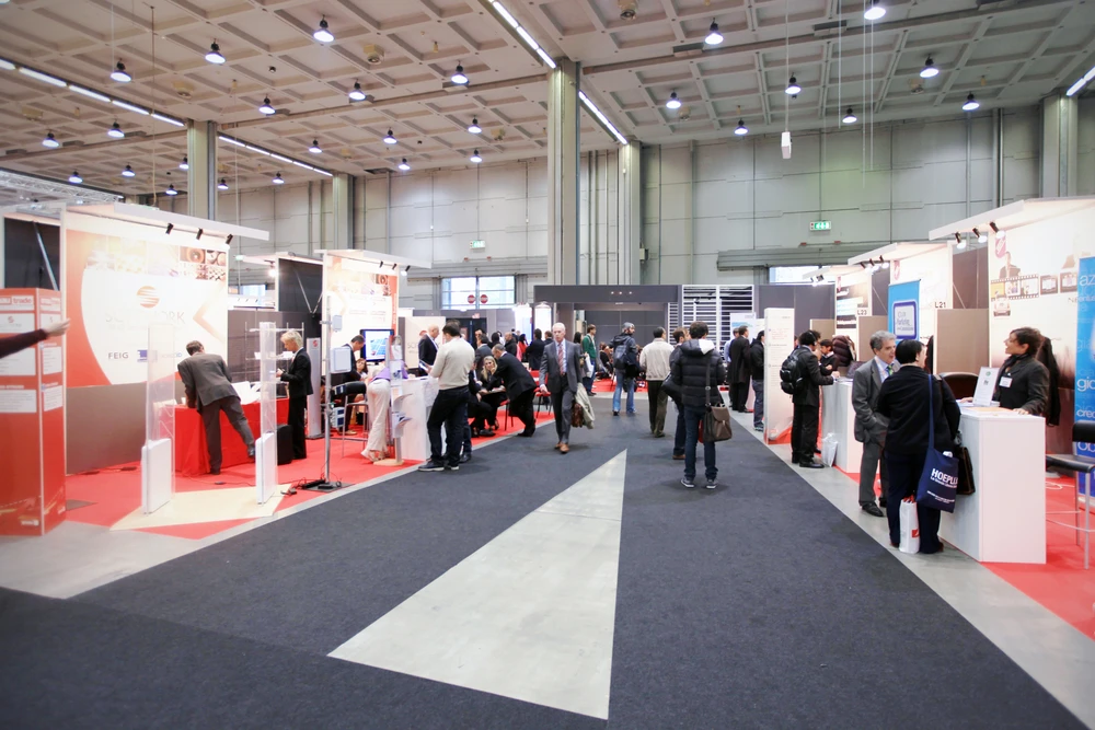 Salon professionnel en intérieur avec stands d'exposition modulaires, visiteurs en tenue d'affaires circulant et échangeant
